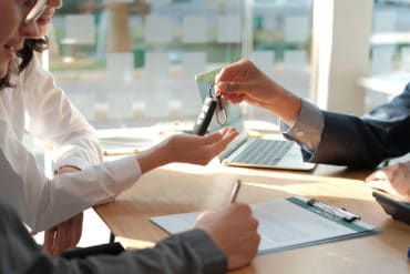 dealer salesman giving car key to new owner. client signing insurance document or rental car lease form