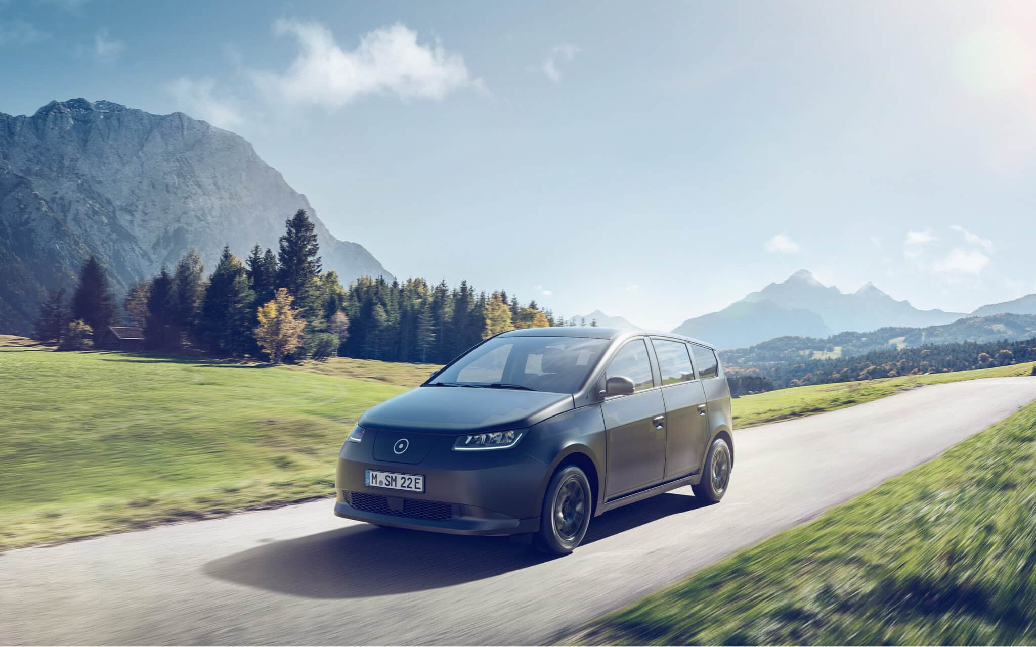 sono motors sion solar-powered ev driving on a road with mountains in the backdrop