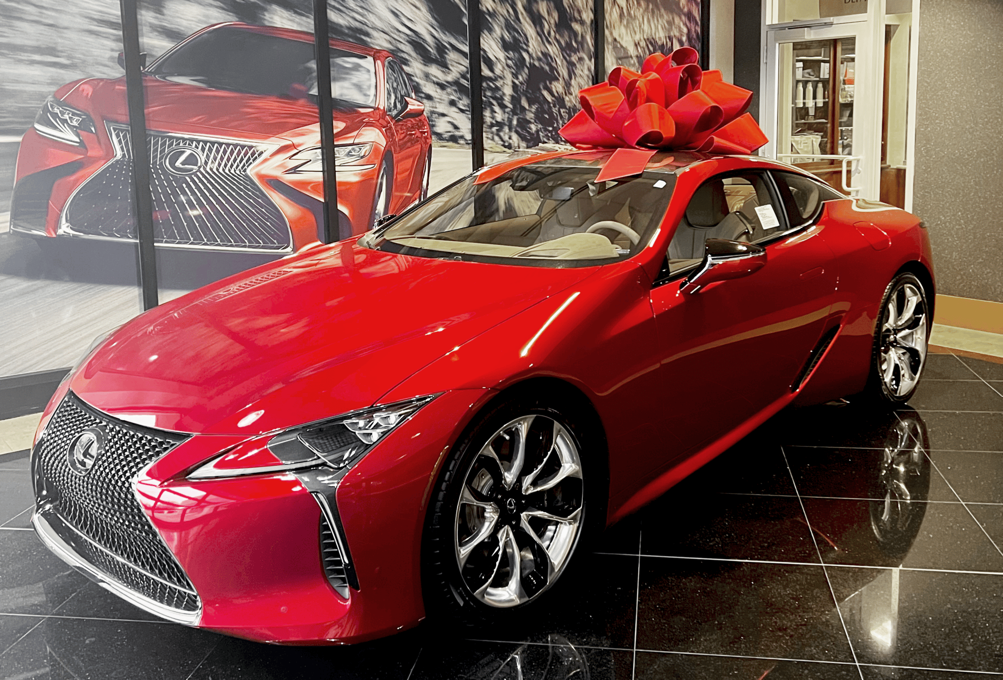 A red Lexus sitting in a showroom with a giant red bow.